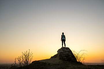 Silhouette of a woman hiker standing alone on big stone at sunset in mountains. Female tourist on...