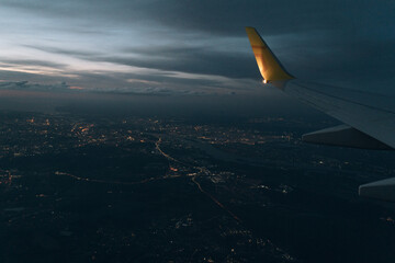 Naklejka na ściany i meble View from the plane on the wing of an airplane flying over the night city