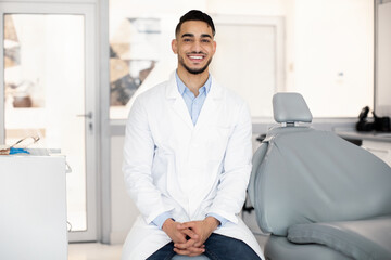 Stomatological Services. Handsome Arab Male Dentist Posing At Workplace In Clinic Interior