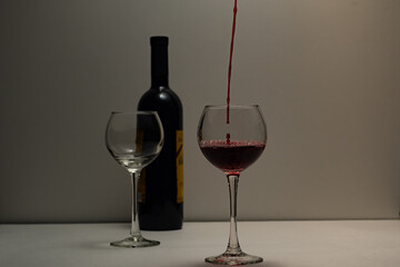 Transparent glasses are filled with red wine, on a holiday. Wine glasses with expensive red wine, bottle, on a light background, romance, Valentine's day, Christmas, new year.