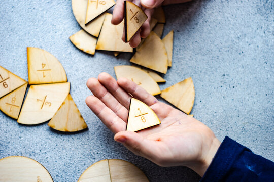 Close-up of a child's hand holding fraction pie chart puzzle pieces