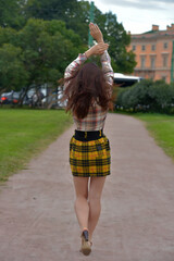 pretty brunette girl in a plaid blouse and skirt on a city street