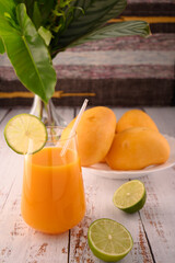 Mango martini and plate of mango and lime. Vase with tropical leaves on left
