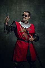 Smiling young man in image of medieval warrior or knight with dirty wounded face using phone...
