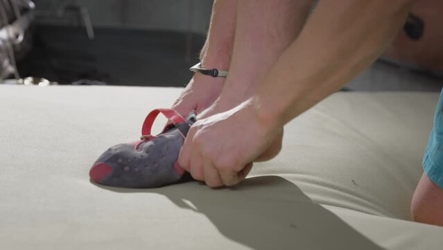 Sporty man rock climber puts on climbing shoes, footwear designed for rock climbing. Pulls boots on his feet. Climbing clothing. Preparing for rock climbing in the gym. Sports hobby in the city