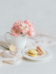 Two tasty French macarons and a jar with pink carnation flowers on a white background.
