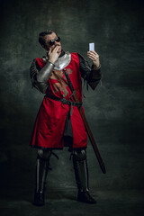 Smiling young man in image of medieval warrior or knight with dirty wounded face using phone...