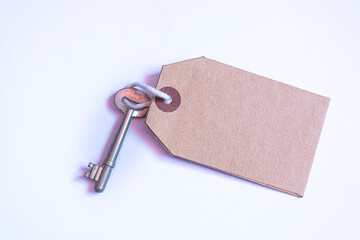 Key and brown paper tag on white background. Flat lay