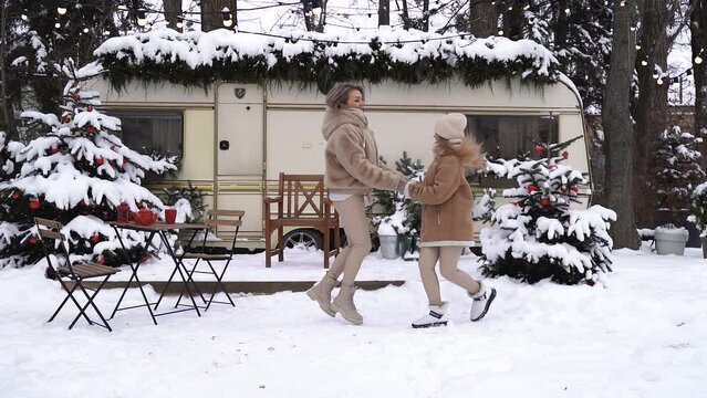 Mom and daughter are jumping in the snow holding hands