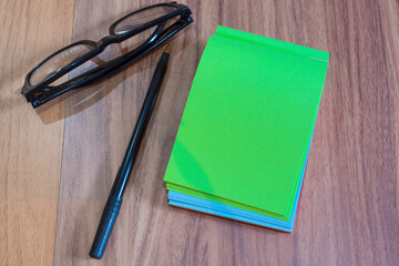 Color notepad with reading glasses and pen on wooden desk. Flat lay