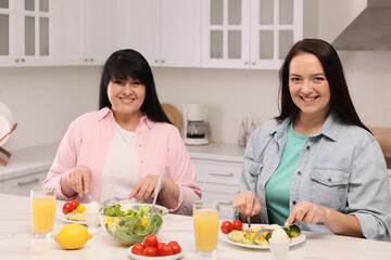 Obraz na płótnie Canvas Happy overweight women having healthy meal together at table in kitchen