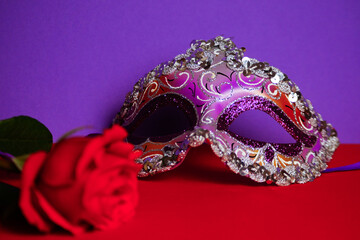 Purple Venetian carnival mask, red rose. Purple-red background .