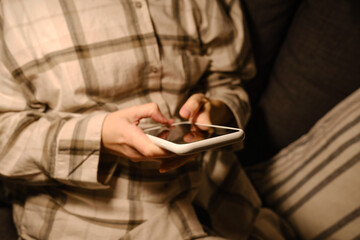 Girl holds a smartphone in her hands in a comfortable bed and checks the social network account before going to bed or after waking up. Gadget addiction. Woman sending text message on mobile phone