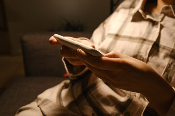 Girl holds a smartphone in her hands in a comfortable bed and checks the social network account before going to bed or after waking up. Gadget addiction. Woman sending text message on mobile phone