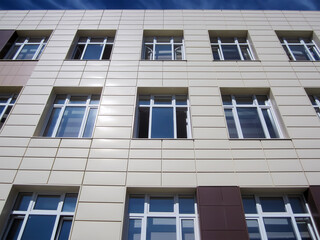 The facade of the building with plastic windows is lined with beige decorative tiles. The windows reflect the blue sky