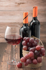 Glass of red wine with grapes on wooden table against the background of bottles