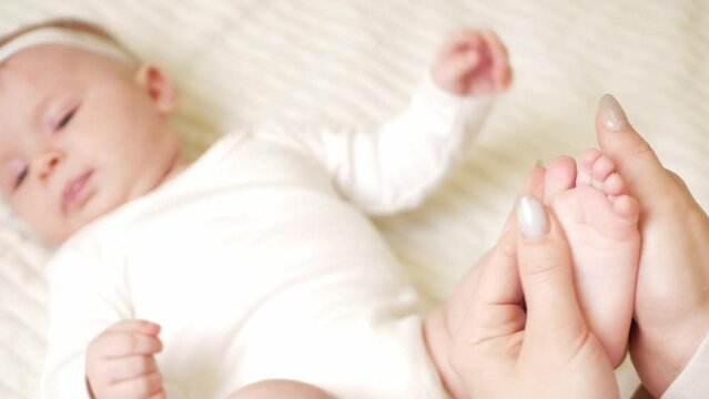 mother massages her little daughter, newborn baby. lies on bed in bedroom, homely. Legs, fingers. haunch