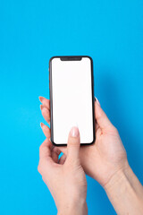 Woman holding mobile phone in two hands with empty white screen on blue background