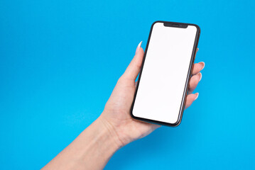 Woman holding mobile phone in hand with empty white screen on blue background