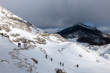 Mountaineers walking, hiking on a winter sunny day to reach the mountain peak. Wind and clouds are...