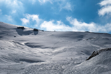 Solo mountaineer walking, hiking on a winter sunny day to reach the mountain peak. Wind and clouds...