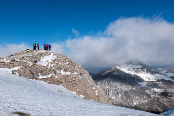 Mountaineers walking, hiking on a winter sunny day to reach the mountain peak. Wind and clouds are...