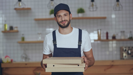 Young delivery man holding pizza boxes at home