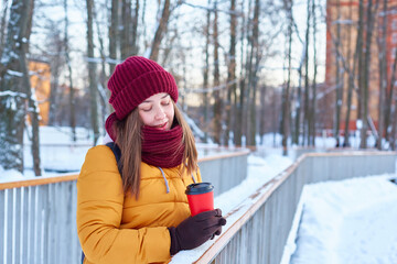 young girl walks in a winter park with a cup of coffee in her hands.