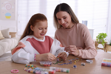 Happy mother with her daughter making beaded jewelry at home