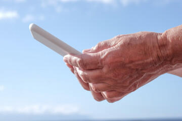 Close-up on human female hands holding a smart phone with white cover. Addiction, woman enjoying technology and social media - rocks beach and waves of sea in background