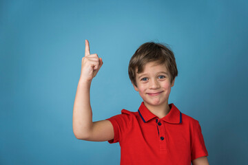 A cute Caucasian boy of 5 years old in a red T-shirt affirmatively and cheerfully points his finger up