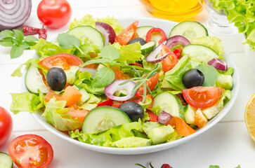 Healthy fresh vegetable salad with tomatoes, cucumbers and bell peppers in a plate on a white wooden background