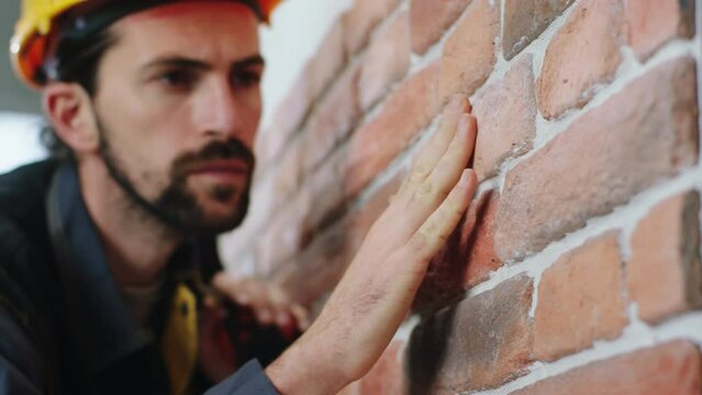 Closeup to the camera carefully constructor worker analysing the new wall built at computer site the wall is from red brick
