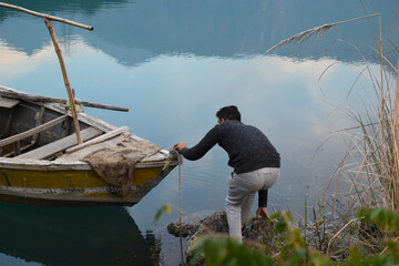 Guy trying to climb on old style rural boat in lake