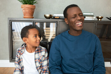 Close-up of two dark-skinned relatives, uncle and his nephew sitting on floor, having fun, spending...