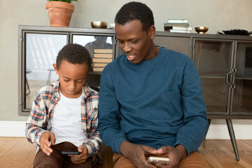 Father and son spending time together after returning home from job and school, sitting against...