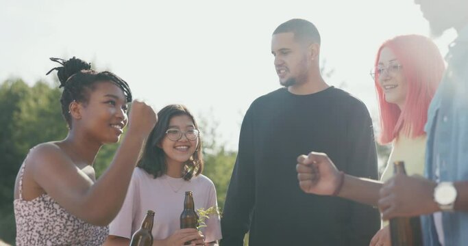 A group of friends of different nationalities spend their time at lake drinking beer from glass bottles, playing rock-paper-scissors, drawing lots to see who will be the driver, betting on something