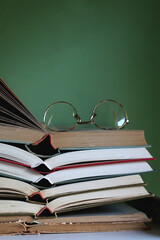 Stack of open vintage hardcover books and retro reading glasses on top. Selective focus.