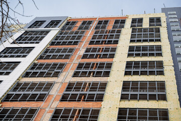 Thermal insulation of a multi-storey building. Insulate the facade of the building. Construction works of a residential building. Tall building, yellow insulation.