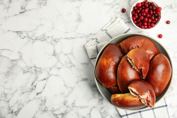 Delicious baked cranberry pirozhki in bowl on white marble table, flat lay. Space for text