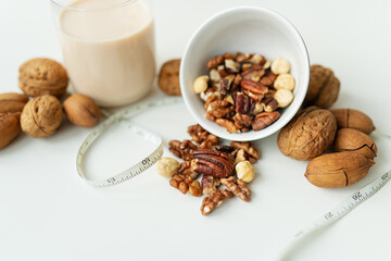 Vegan milk from nuts in a glass cup with various nuts on a white table. Nuts in a bowl. Low-calorie milk for body support.