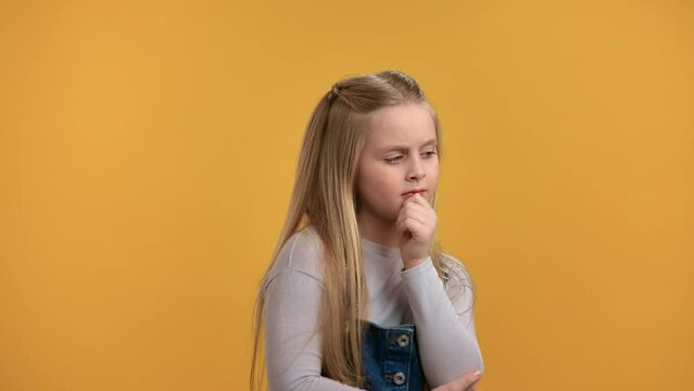 Smart pensive female little kid thinking solving problem making choice posing isolated on orange 