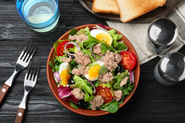 Bowl of delicious salad with canned tuna and vegetables served on black wooden table, flat lay