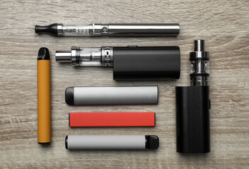 Different electronic cigarettes on wooden background, flat lay