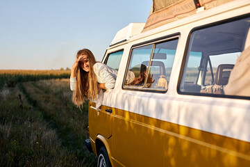 On the way to unknown places. Attractive young woman leaning out the vans window, enjoying the car...