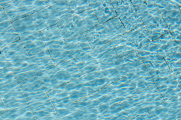 Beautiful texture of water with sun lights in a pool on the blue background of texture of small square ceramic tile