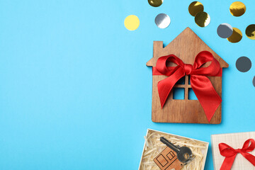 Wooden house model and key in gift box on light blue background, flat lay with space for text. Housewarming party