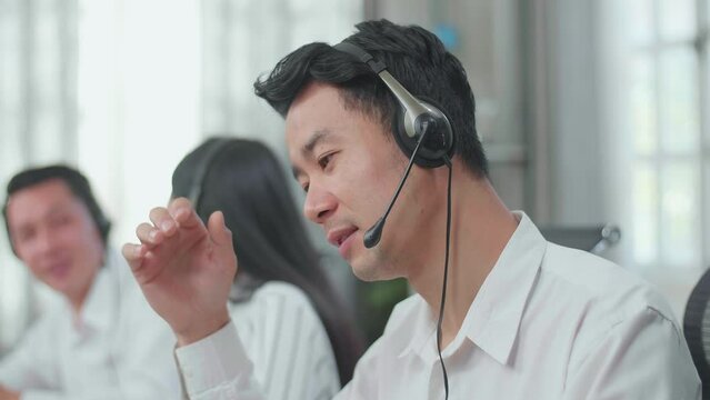 A Man Of Three Asian Call Center Agents Wearing Headset Tired Because Two Of His Colleagues Are Talking During Working At The Office
