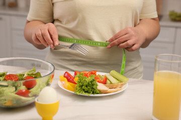 Obraz na płótnie Canvas Overweight woman measuring waist while having meal at home, closeup