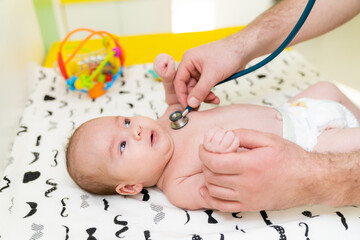 Woman pediatrician is examining little baby in clinic. Baby's diagnosing. Nurse listening child...